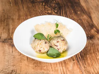 a white plate with two meatballs on a wooden table at Muliné Lodge in Selva di Val Gardena