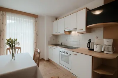 a kitchen with white cabinets and a table with a vase of flowers at Apartment Hotel Elvis in Ortisei