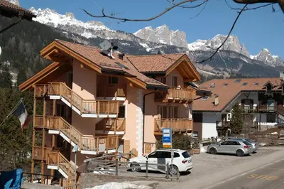 a building with cars parked in front of it with mountains at Casa Sandra Moena by Go new Location in Moena