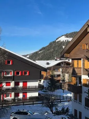 a building with red windows and a snow covered mountain at Appartamento ai piedi delle Dolomiti in Selva di Val Gardena