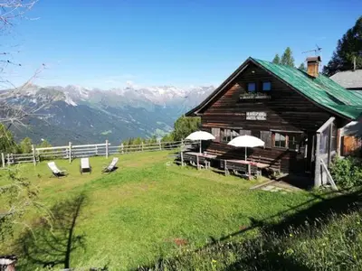 a log cabin with chairs and umbrellas on a field at Hühnerspielhütte - Rifugio Gallina - Mountain Hut Hühnerspielhütte in Moncucco