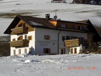 a house with wooden balconies on a snow covered slope at Pension Aichner in Terento