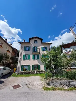 a large white building with green shutters at Appartamento Vecchia Osteria in Rocca Pietore