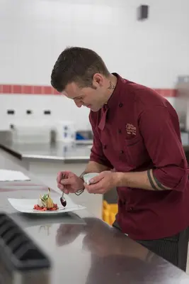 a man in a kitchen preparing a plate of food at Pension Garden Hotel in Colfosco