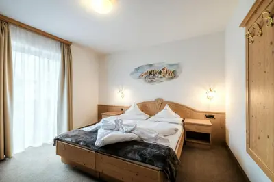a bedroom with a bed with white sheets and a window at Hotel Else in Selva di Val Gardena