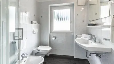 a white bathroom with a toilet and a sink at Hotel Else in Selva di Val Gardena