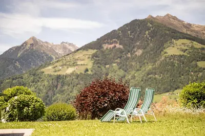 two chairs sitting in the grass with mountains in the background at Hotel Garni Alpes in Schenna