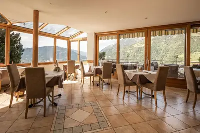 a dining room with tables and chairs and windows at Hotel Garni Alpes in Schenna