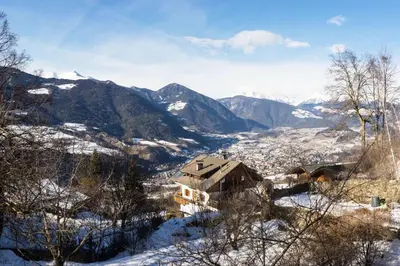 a house on a snowy hill with mountains in the background at Large apartment with panoramic view in Meluno