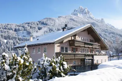 a house in the snow with a mountain in the background at Hotel Villa Mozart in Pozza di Fassa