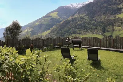 two chairs in a yard with a fence and mountains at Haslingerhof - Ferienwohnung Hirzer in Saltusio