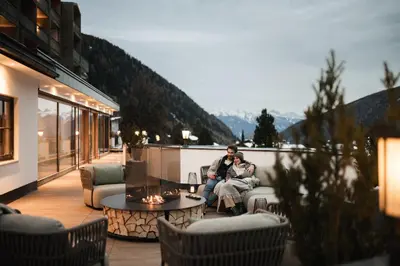 a man and woman sitting on a patio at Falkensteiner Hotel Falkensteinerhof l 4 Star Superior in Valles