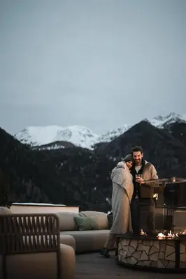 a man and a woman sitting on a couch with mountains in the background at Falkensteiner Hotel Falkensteinerhof l 4 Star Superior in Valles
