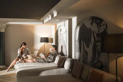 a man and woman sitting on a couch in a living room at Falkensteiner Hotel Falkensteinerhof l 4 Star Superior in Valles