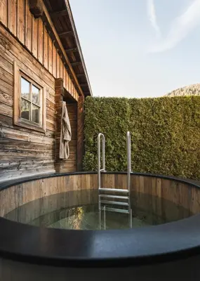 a hot tub in front of a building with a chair at Falkensteiner Hotel Falkensteinerhof l 4 Star Superior in Valles