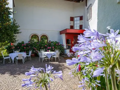 a patio with tables and chairs and purple flowers at Hotel Mühle Mayer in Termeno