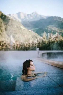a woman swimming in a pool with mountains in the background at Vitalpina Hotel Waldhof in Rablà