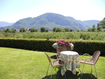 two chairs and a table in a yard with mountains at Gardenhotel Premstaller in Bolzano