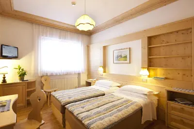 a bedroom with two beds and a desk and a window at Hotel Bellaria - Cortina d'Ampezzo in Cortina dʼAmpezzo