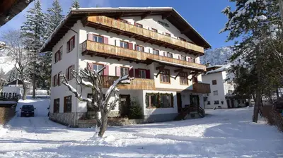 a building in the snow with a tree at Hotel Bellaria - Cortina d'Ampezzo in Cortina dʼAmpezzo