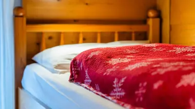 a bed with a red blanket on top of it at Alpen Suite Apartment in San Vigilio Di Marebbe