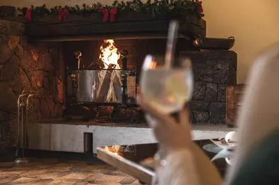 a person holding a glass of wine in front of a fireplace at G. Hotel Des Alpes (Classic since 1912) in San Martino di Castrozza