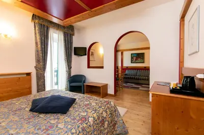 a bedroom with a bed and a living room at G. Hotel Des Alpes (Classic since 1912) in San Martino di Castrozza