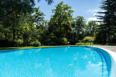 a blue swimming pool with trees in the background at Flow Apartments WINKEL STUDIO in Merano