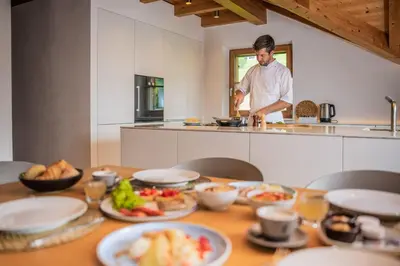 a man preparing food in a kitchen with plates of food on a table at Tagenhof Mountain Living in Meluno