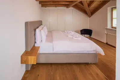 a bedroom with a bed with white sheets and a chair at Tagenhof Mountain Living in Meluno