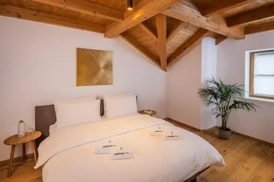 a bedroom with a large white bed with wooden ceilings at Tagenhof Mountain Living in Meluno