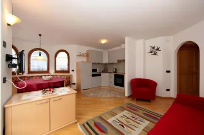 a living room with a red chair and a kitchen at Cesa Mattias - Appartamenti a Canazei in Canazei