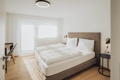 a white bedroom with a large bed and a desk at Apart Suites Gravbach in Lagundo