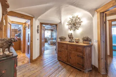 a living room with a wooden floor and a room with a chandelier at Casa Cristallino, in centro con balcone panoramico in Cortina dʼAmpezzo
