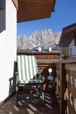 a rocking chair on a balcony with mountains in the background at Casa Cristallino, in centro con balcone panoramico in Cortina dʼAmpezzo