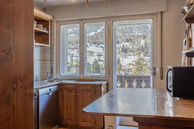 a kitchen with a counter and two large windows at Casa Cristallino, in centro con balcone panoramico in Cortina dʼAmpezzo