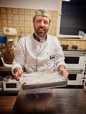a man in a kitchen holding a pan of food at Cafe Rudi Living Apartements in Parcines