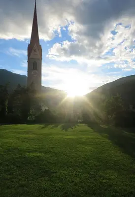 a church steeple in a field with the sun shining at Hotel Föhrenhof in Naz-Sciaves