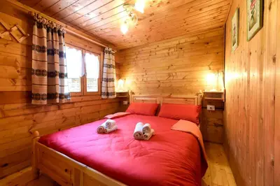 two stuffed animals sitting on a red bed in a wooden room at Fienile Rustico Alleghe Tabià in Alleghe