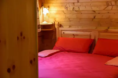 a bedroom with a bed with red sheets and a wooden wall at Fienile Rustico Alleghe Tabià in Alleghe