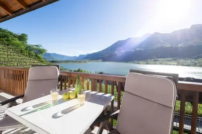 a table and chairs on a balcony with a view of a river at Ferienwohnungen Fuchsleitenhof am See in Caldaro