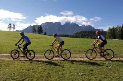 three people riding bikes on a grassy field at Mountain Residence CLARA in Riscone