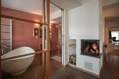 a living room with a fireplace and a tub at Taubers Unterwirt Aktiv & Vitalhotel in Feldthurns