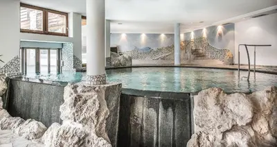 a swimming pool in a building with a rock wall at Taubers Unterwirt Aktiv & Vitalhotel in Feldthurns