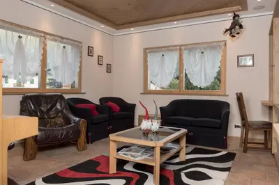 a living room with black leather chairs and a table at Garnì Val de Grepa in Pozza di Fassa