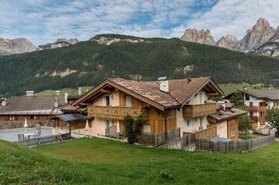 a house on a hill with mountains in the background at Garnì Val de Grepa in Pozza di Fassa