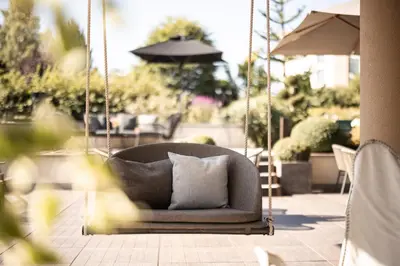 a couch swinging on a patio with an umbrella at DER MESNERWIRT - 4 Superior - Meraner Land in Avelengo