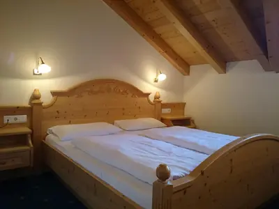 a bedroom with a large wooden bed with white sheets at Hotel Jú Furcia in San Vigilio Di Marebbe