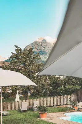 two white umbrellas and a pool with a mountain at Hotel Turmwies in Tirolo