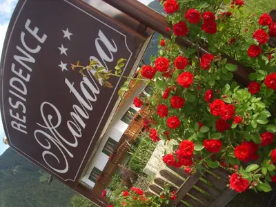a sign in front of a building with red flowers at Apartments Residence Montana in Rasun di Sopra
